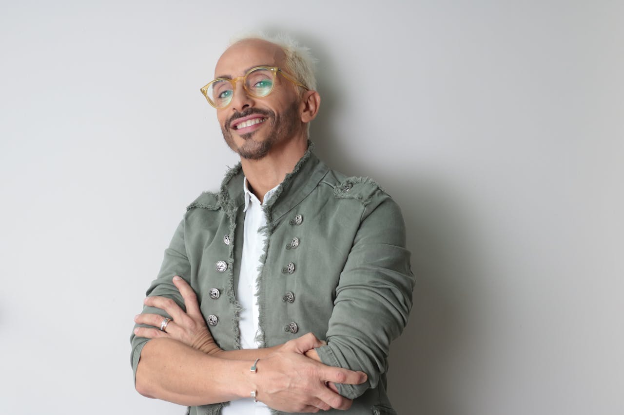 Services-03 Chic mature man with glasses and stylish jacket confidently posing indoors against a plain background.